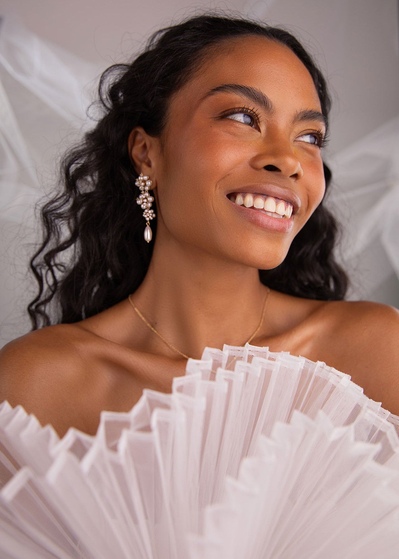 Woman wearing a white off-shoulder dress with ruffled details, smiling against a neutral background.