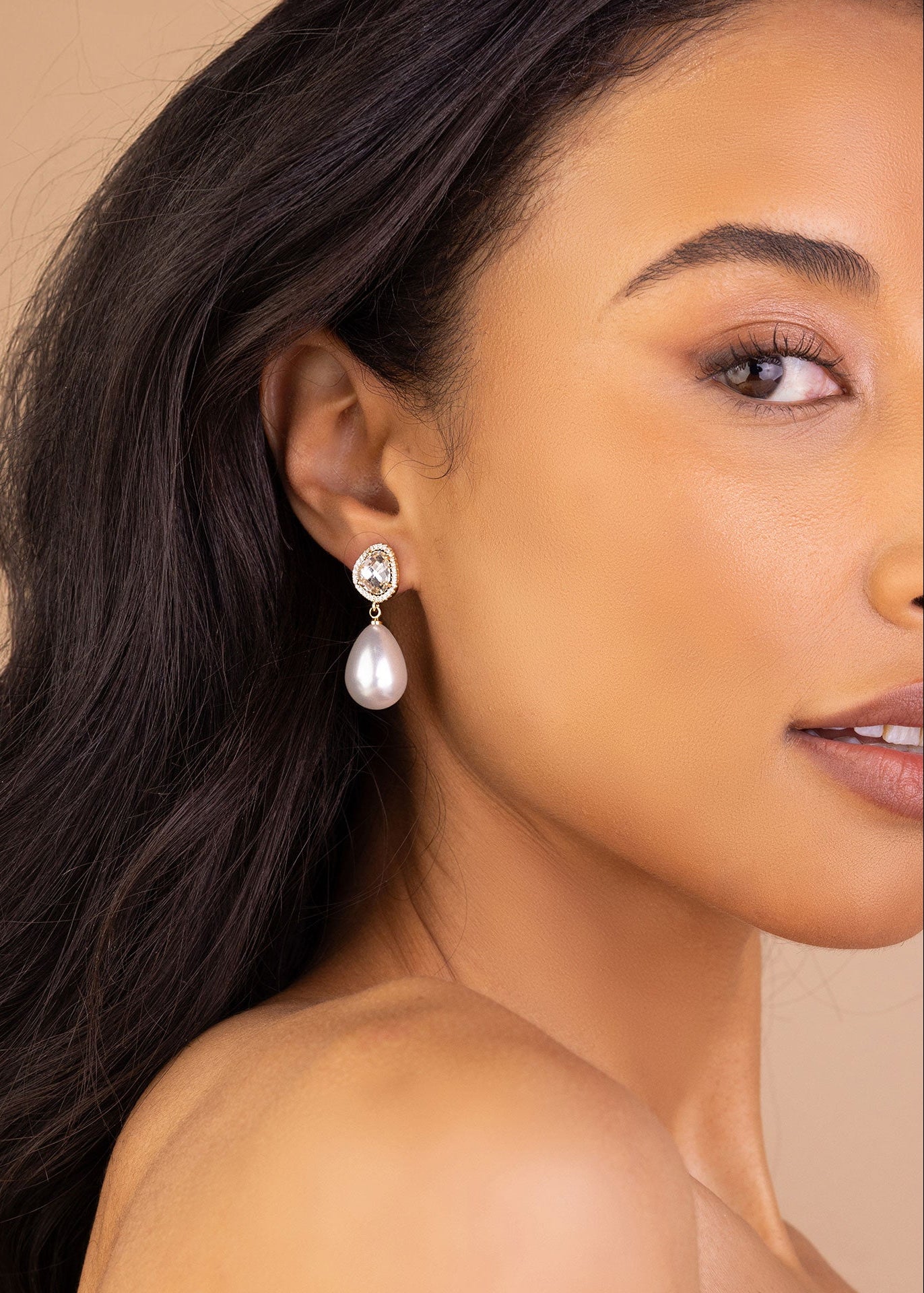 Close-up of a woman wearing pearl earrings with a neutral background